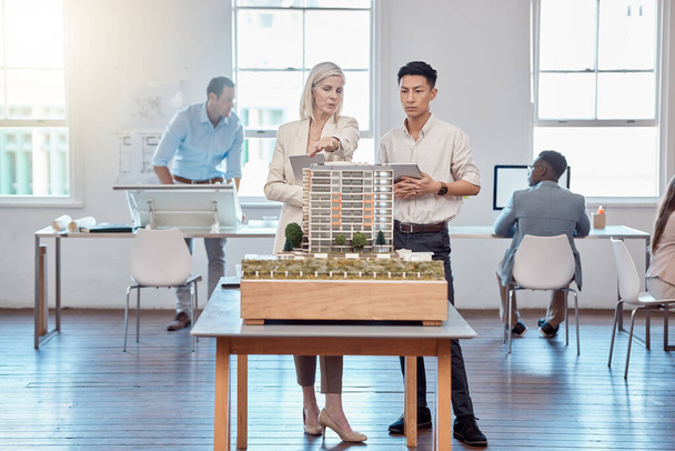 Confident business professionals in the field of architecture working together on building designs in a modern office. Team of male and female architects talk over a model construction for a project - Photo, image