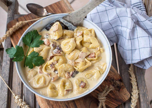 Tortellini alla panna. Traditional and homemade fresh cooked italian pasta dish. Served in a bowl with spatula on wooden background - Photo, image