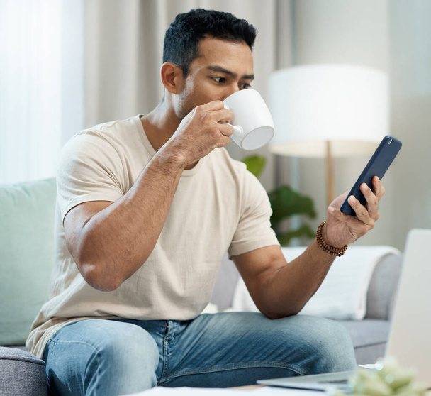 Social media is my morning news. a young man sitting in his living room and using his cellphone while enjoying a cup of coffee - Photo, image