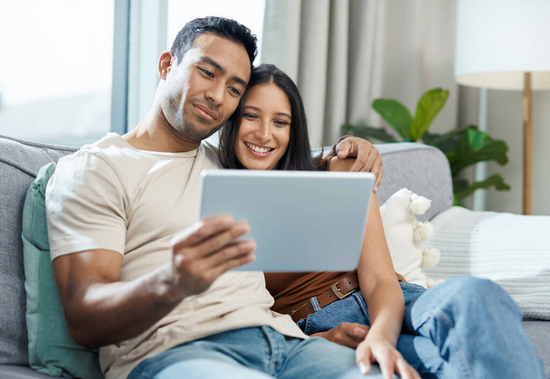 This is our favourite show to watch. a young couple sitting on the sofa together at home and using a digital tablet - Fotoğraf, Görsel