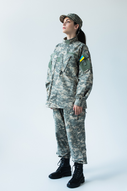 Full length of servicewoman in uniform with ukrainian flag on grey background - 写真・画像