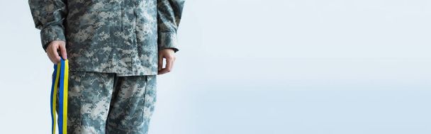 Cropped view of servicewoman in military uniform holding blue and yellow ribbon isolated on grey, banner  - Photo, image