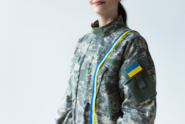 Cropped view of smiling soldier in uniform with blue and yellow ribbon and ukrainian flag isolated on grey  - Photo, image