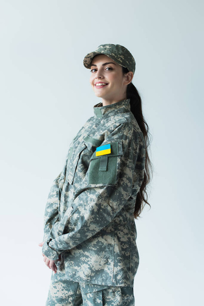 Positive soldier in cap and uniform with ukrainian flag isolated on grey  - Photo, Image