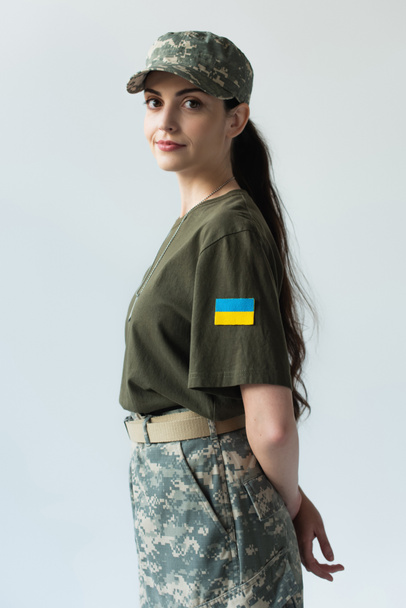 Young soldier with ukrainian flag on chevron looking at camera isolated on grey  - Photo, Image