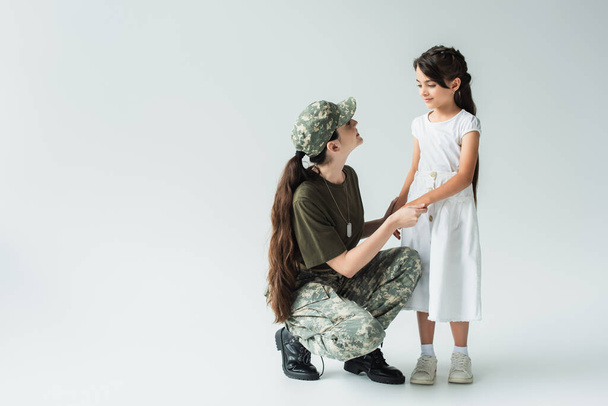 Smiling woman in military uniform holding hands of daughter on grey background - Foto, immagini