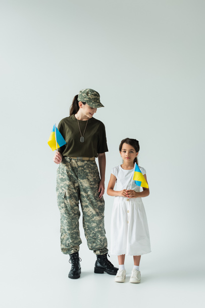 Soldier holding ukrainian flag near daughter on grey background - 写真・画像