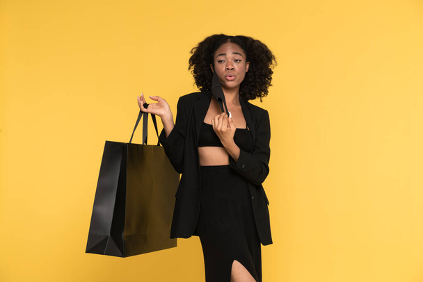 Black young woman posing with shopping bag and face mask isolated over yellow background - Foto, Imagem