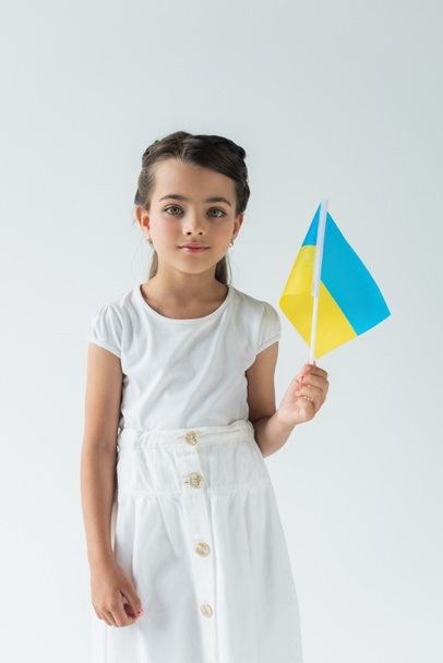 Girl holding ukrainian flag and looking at camera isolated on grey  - Fotografie, Obrázek