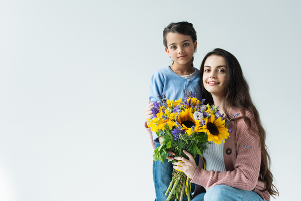 woman and girl smiling at camera near bouquet of blue and yellow flowers isolated on grey - Фото, зображення
