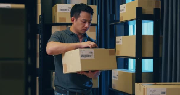Asian businessman stand front of shelf check online data information detail on digital tablet compare with cardboard box for express delivery in warehouse at night. Startup small business concept. - Filmmaterial, Video