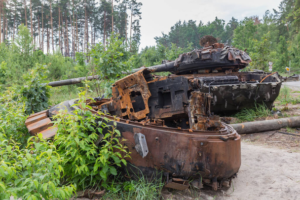 Russian tank destroyed during hostilities in Russian invasion of Ukraine, 2022 and torn down gun turret of another tank on a foreground on a forest edge next a road. - Foto, imagen