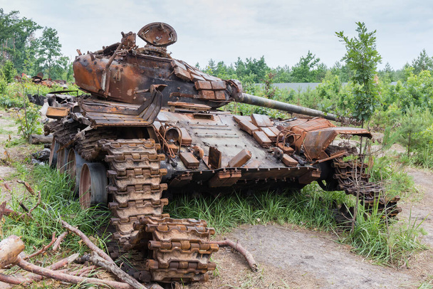 Venäläinen tankki tuhoutui ja paloi vihollisuuksien aikana Venäjän hyökkäyksessä Ukrainaan vuonna 2022. Seisoo nuorten puiden keskellä metsän reunalla.  - Valokuva, kuva