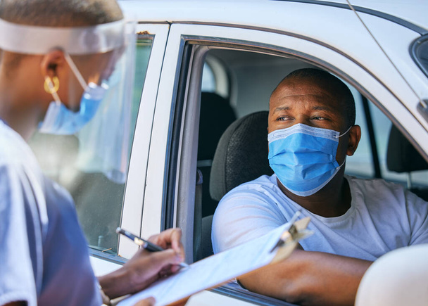 Test, questions and screening at a covid drive thru checkpoint. A man traveling in a car talking to a healthcare professional writing his coronavirus details while wearing a face mask. - Photo, Image