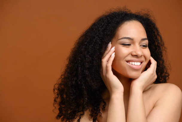 Natural beauty. Portrait of charming multiracial lady standing against brown wall. Young beautiful black woman isolated on brown background smiles toothy and looking away - Foto, immagini