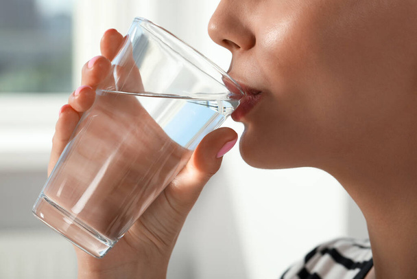 Young woman drinking water indoors, closeup. Refreshing drink - Фото, зображення