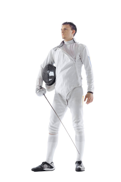Portrait of professional male fencer in fencing costume and mask holding smallsword isolated on white background. Athlete practicing in motion, action. Copyspace for ad. - Photo, Image