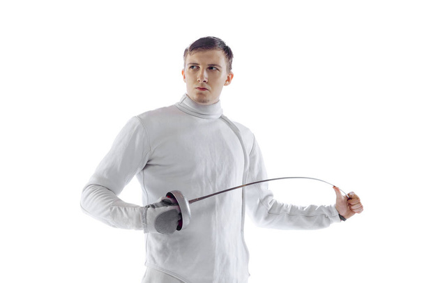 Portrait of professional male fencer in fencing costume and mask holding smallsword isolated on white background. Athlete practicing in motion, action. Copyspace for ad. - Foto, afbeelding