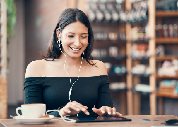 Beautiful, happy and relaxed student listening to a podcast, education video or music in cafe on a tablet. Smiling woman browsing online and watching distance learning webinar in restaurant. - Photo, Image
