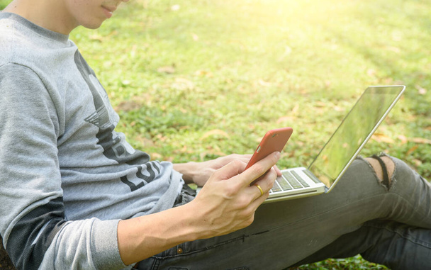 Młody człowiek z telefonem i laptopem na zewnątrz - Zdjęcie, obraz