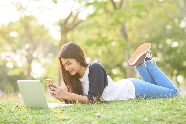 Привлекательная девушка играет мобильный телефон с ноутбуком в саду - Фото, изображение