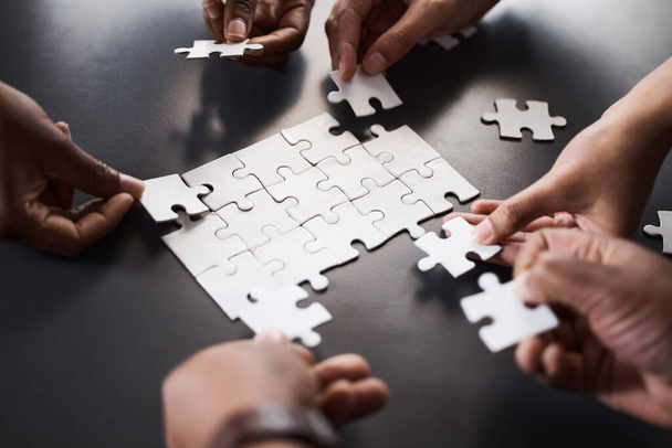 We can figure it out faster if we work together. Closeup shot of a group of unrecognisable businesspeople joining puzzle pieces together in an office - Фото, зображення
