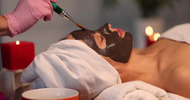 The cosmetologist applies a mask with a brush on the face of a lying woman, close-up. Chocolate face mask - Footage, Video