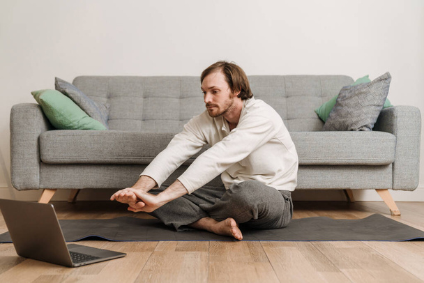 Ginger man using laptop during yoga practice on floor at home - Foto, afbeelding