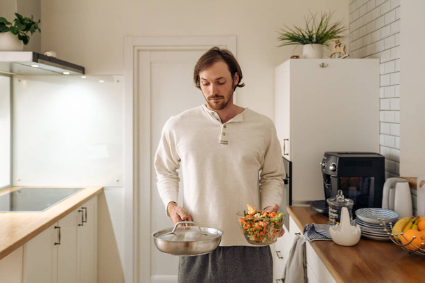 Ginger bristle man making dinner with vegetables in kitchen at home - 写真・画像