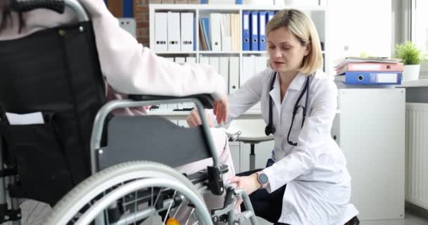 Kadın bir doktor, tekerlekli sandalyedeki bir kadının dizine çekiçle vuruyor. Sakatlık sonrası refleksi kontrol ediliyor. - Video, Çekim