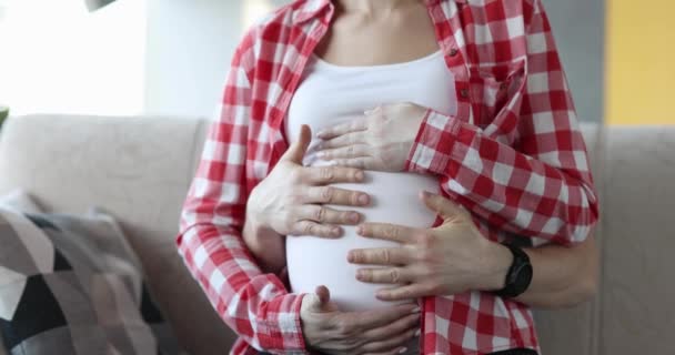 Mannelijke handen streelden de buik van een zwangere vrouw, close-up. Wachten op de geboorte van een kind, familie - Video