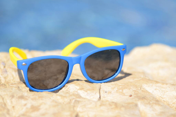 Resort vacation concept - close-up blue yellow sunglasses on stones a bright sunny day by the pool - copy space - Valokuva, kuva