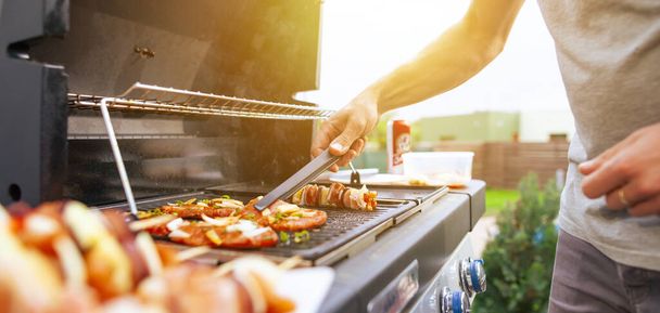 Young man grilling some kind of meats on a gas grill during lovely summer time, food concept - Photo, image
