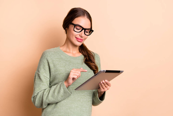 Photo of cute shiny girl dressed green pullover eyewear typing modern device empty space isolated beige color background. - 写真・画像