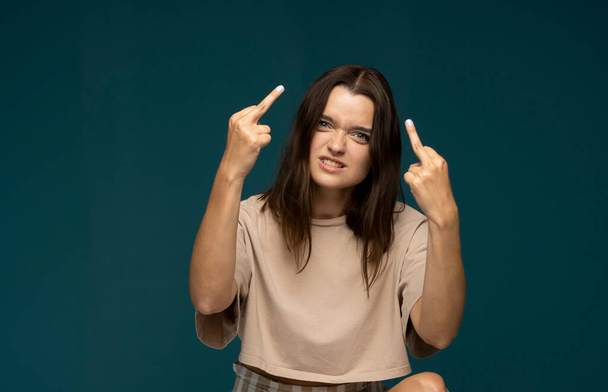 Portrait of brunette student woman showing middle finger doing rebel expression at camera standing in studio with blue background - Photo, image