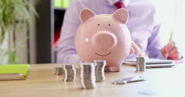 There is a pink piggy bank and coins on the table in the office, close-up. Distribution of profits, income from the deposit - Imágenes, Vídeo