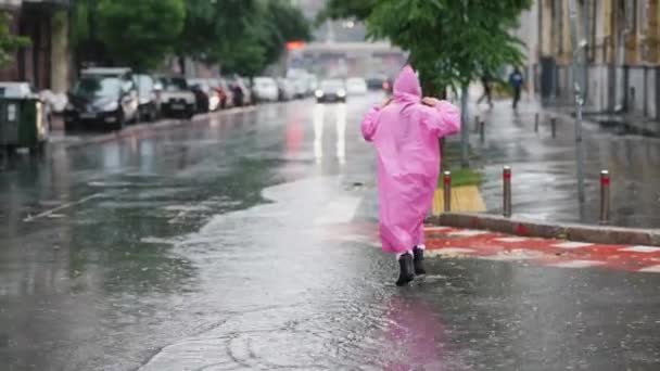 Młoda uśmiechnięta kobieta w różowym płaszczu przeciwdeszczowym na ulicy podczas spaceru po mieście w deszczowy dzień. - Materiał filmowy, wideo