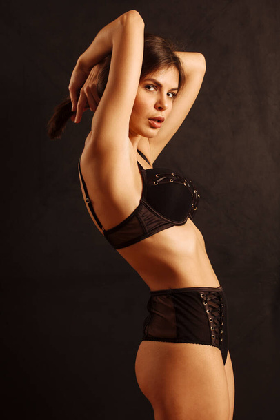 Sexy young woman posing in black underwear over a dark background. - 写真・画像