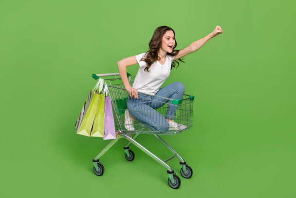 Photo of funny hurrying young lady wear white t-shirt driving tray rising fist isolated green color background. - 写真・画像