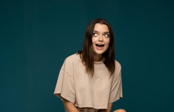 Young pretty brunette woman cute face expression posing in beige t-shirt on blue background isolated, emotional, funny - Fotó, kép