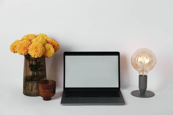 Blank screen laptop and vase with dahlia flowers on table. Home office concept. Designated work from home area. Close up, copy space, background. - Fotó, kép