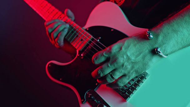 Rock guitarist man on smoky stage masterfully playing electrical guitar. Musician plays music during concert under neon colorful light. High quality photo - Φωτογραφία, εικόνα