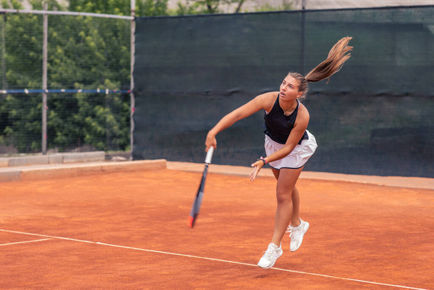 In a luminous summer day on the professional tennis court good looking woman playing the tennis she hitting the ball very hard with the racket. - Fotó, kép