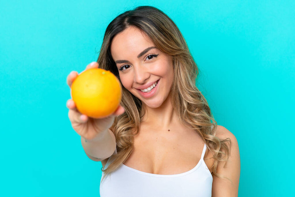 Молодая белая женщина на голубом фоне держит апельсин - Фото, изображение