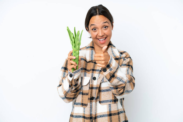 Young hispanic woman holding a green beans isolated on white background with thumbs up because something good has happened - Fotoğraf, Görsel