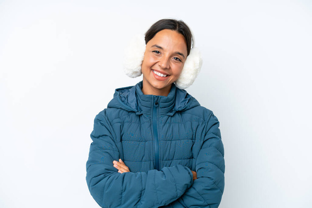 Young hispanic woman wearing a winter earmuffs isolated on white background posing with arms at hip and smiling - Foto, Imagen