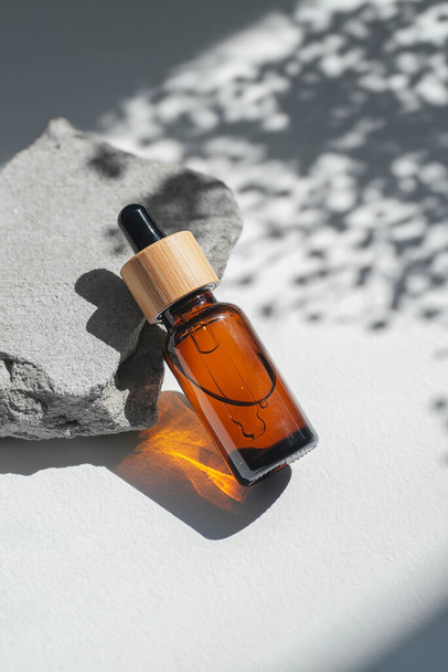 Amber dropper bottles with serum, tonic or essential oil on grey concrete podium. White background with daylight with flowers shadows. Beauty concept for face and body care - Valokuva, kuva