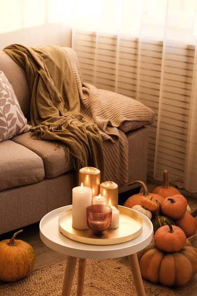 Bunch of pumpkins of different kinds, shapes and colors on the floor and a table near the couch of a living room. Symbol of autumnal holidays with a lot of copy space for text, close up, background. - Foto, afbeelding