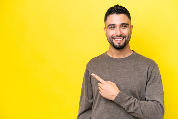 Young Arab handsome man isolated on yellow background pointing to the side to present a product - Φωτογραφία, εικόνα