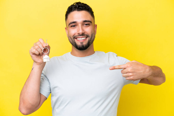 Young Arab man holding home keys isolated on yellow background with surprise facial expression - Φωτογραφία, εικόνα